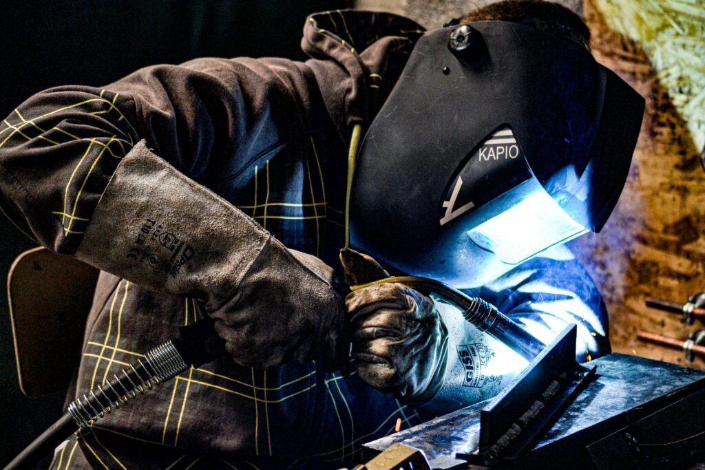 A male welder operates in a factory setting, using protective gear for safety.