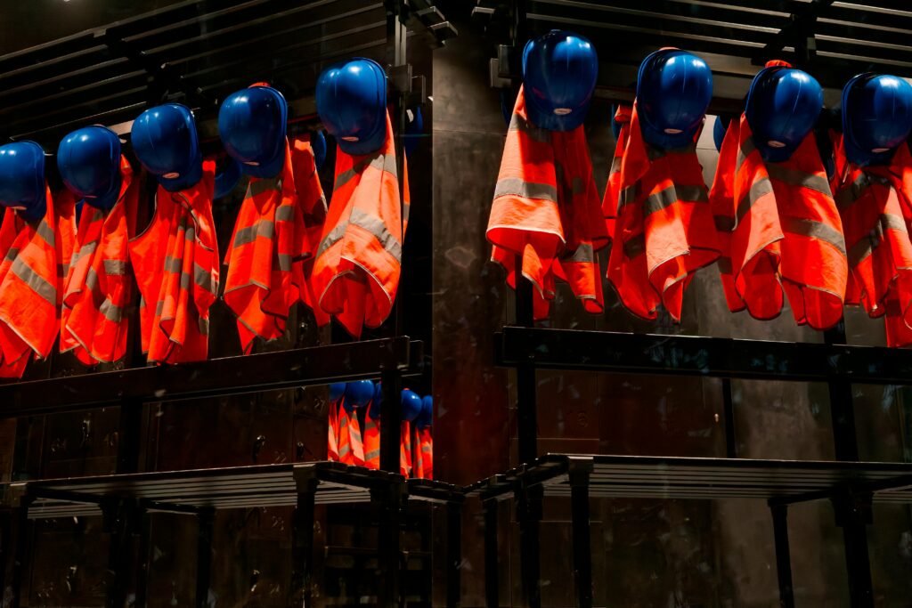 Row of orange safety vests and blue helmets hanging in industrial setting